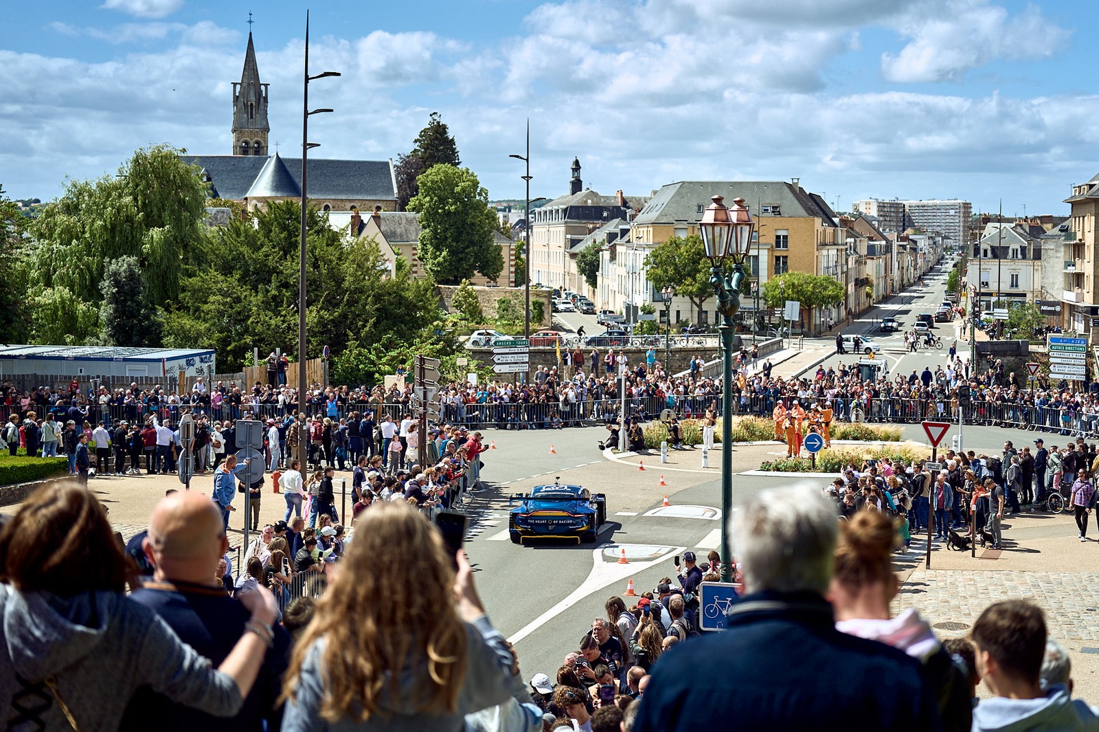Voiture de course paradant dans les rues du Mans devant une foule dense, ambiance des 24 Heures
