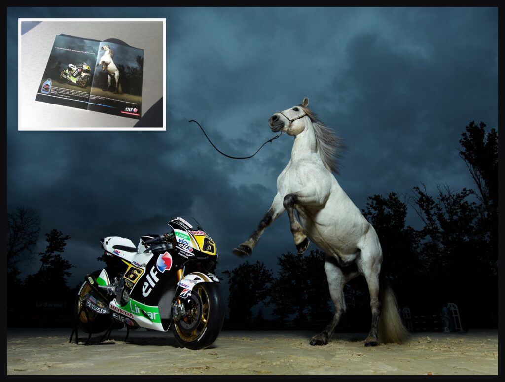 Campagne mondiale ELF 2014 — moto Honda LCR MotoGP face à un cheval blanc cabré sous un ciel d'orage au Mans, avec la parution presse ELF (magazine italien) en médaillon